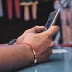 Detailed view of a hand with a tattoo holding a smartphone indoors, showcasing modern technology.