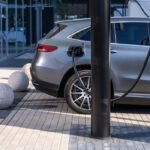 A silver electric car charging at an urban station, highlighting sustainable living in a modern cityscape.