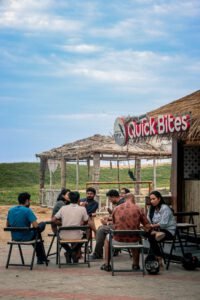 A group of adults seated outside a Quick Bites cafe, sharing a casual moment together under a clear sky.
