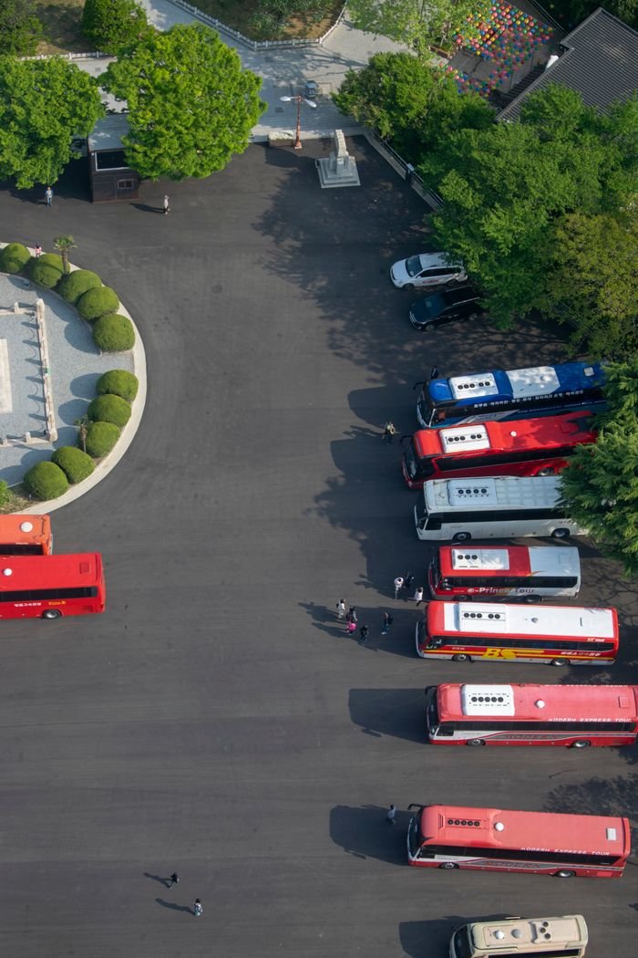High-angle view of multiple buses parked in an orderly row in a clear outdoor parking area.