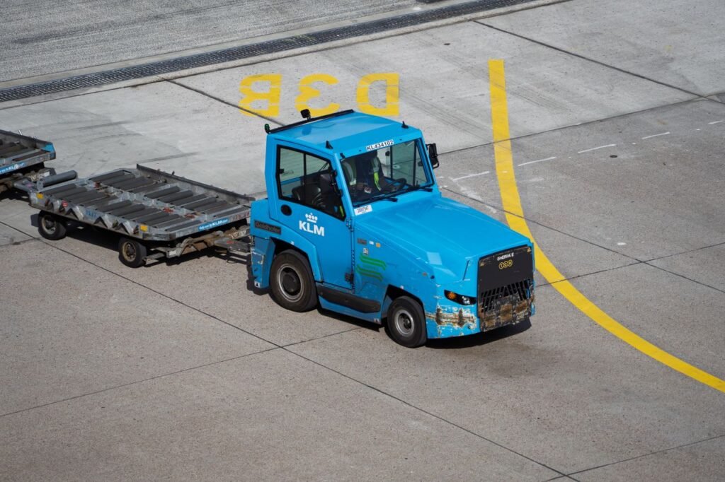 Industry Vehicles KLM Ground Support Equipment towing baggage carts on airport tarmac.