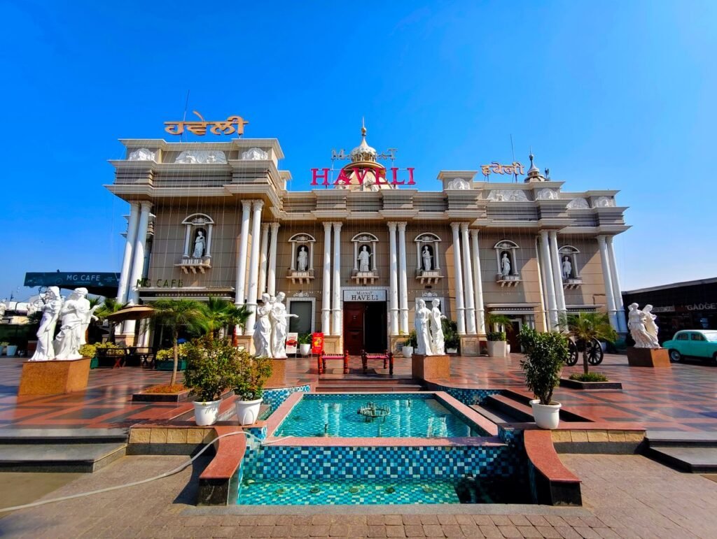 pexels-photo-34988205-34988205 Exterior of the Haveli restaurant with statues and fountain under a clear blue sky.