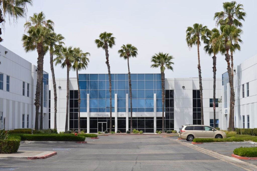 Office Building Contemporary glass office building with palm trees and a parked car in daylight.